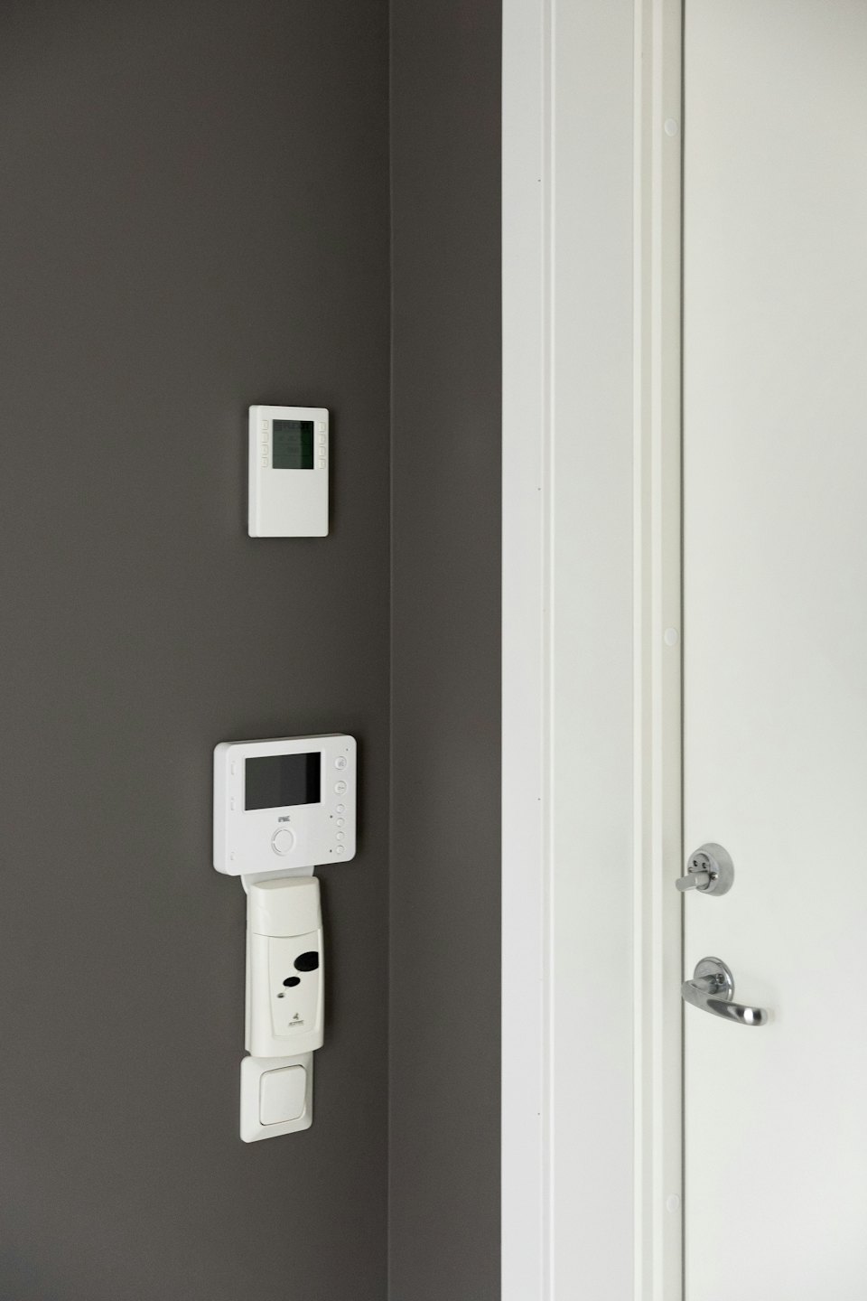 Smart home control devices mounted on a wall beside a door.