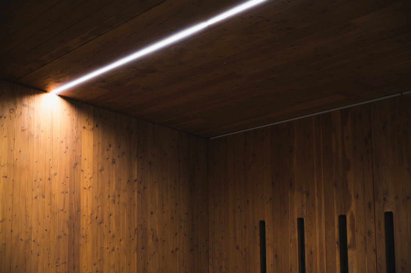 Modern wooden paneled walls meet at a corner with integrated lighting.